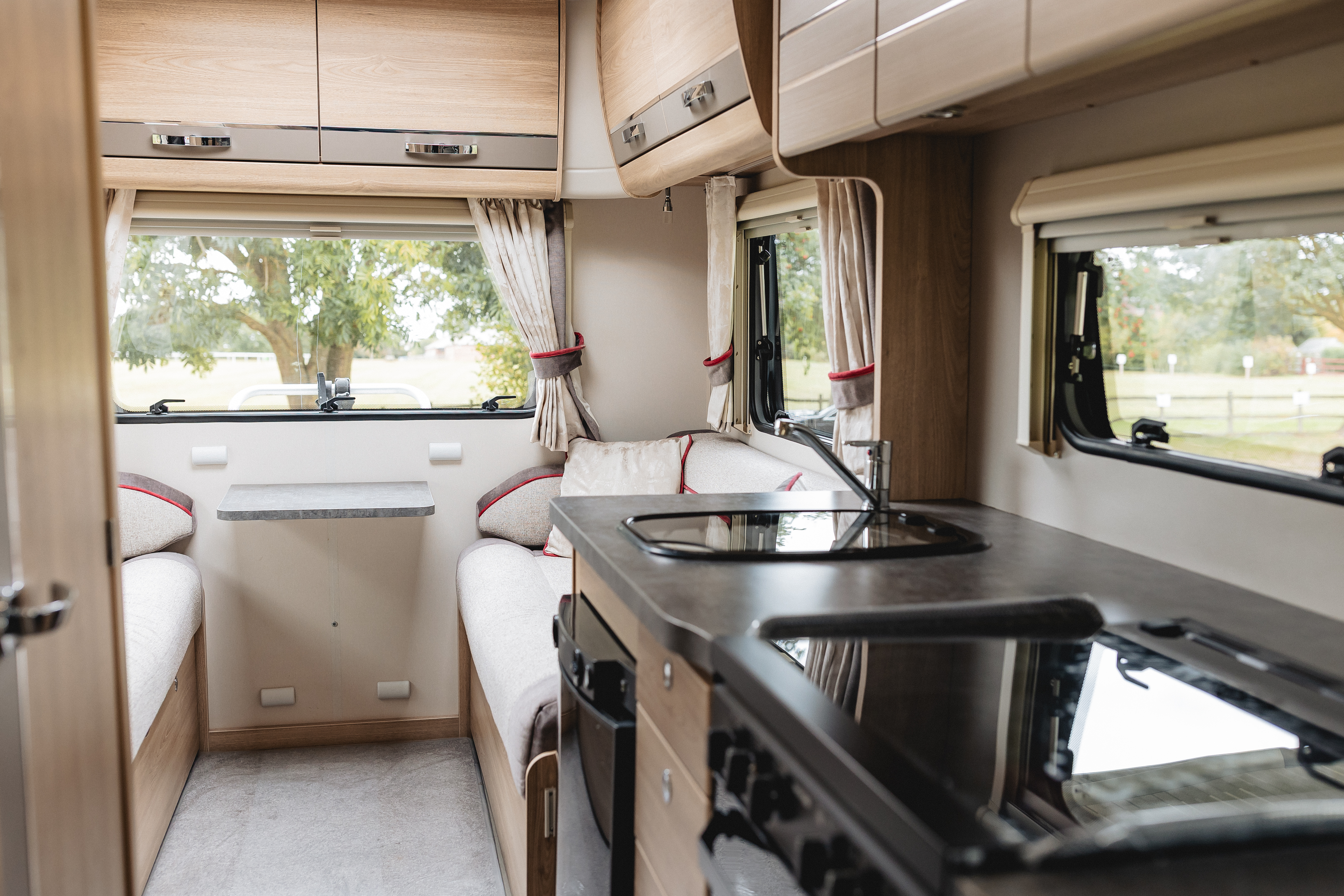 Interior view of a modern motorhome featuring a kitchen area with a sink and stove, seating on either side, and large windows allowing natural light.
